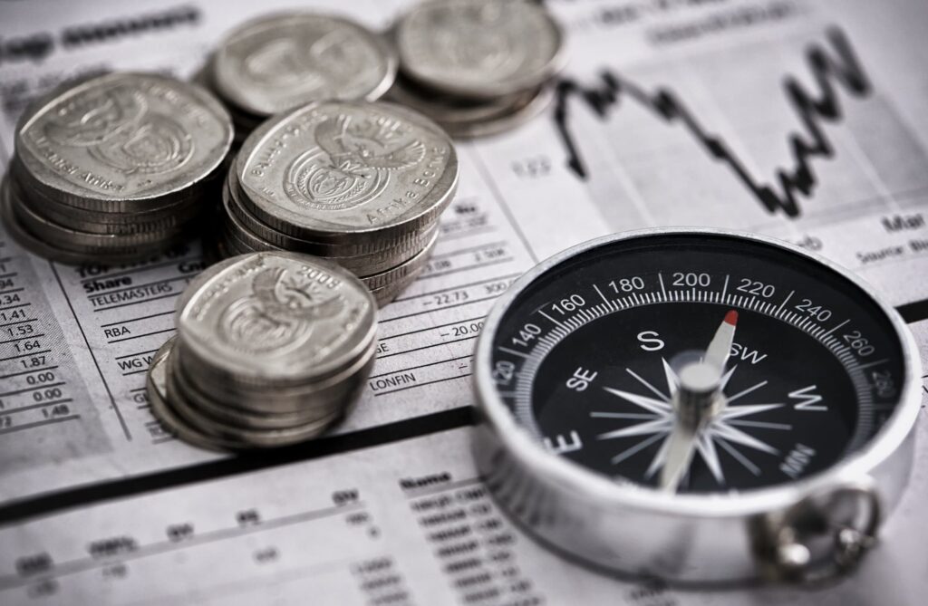 Monedas, una brújula y el gráfico de un periódico financiero